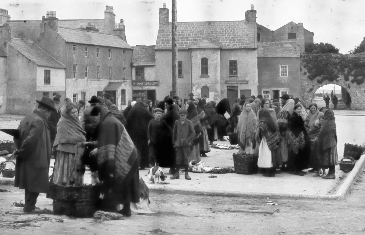 Una multitud en un mercado de pescado irlandés; la mayoría de las mujeres llevan chales oscuros echados sobre la cabeza