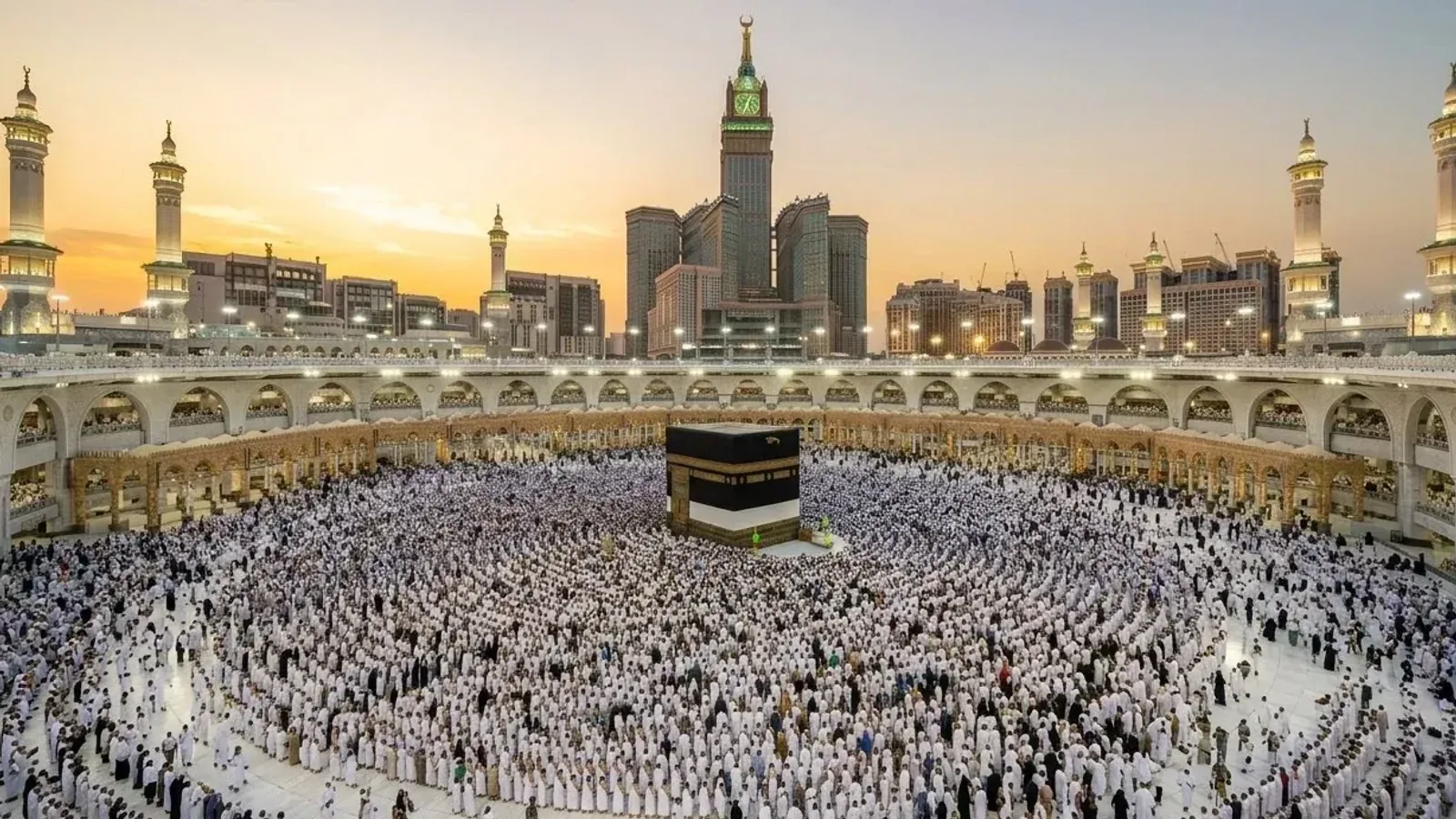 The Kaaba in the Sacred Mosque in Mecca at sunset, ringed by rows of worshippers in white, with the minarets and the clock tower behind
