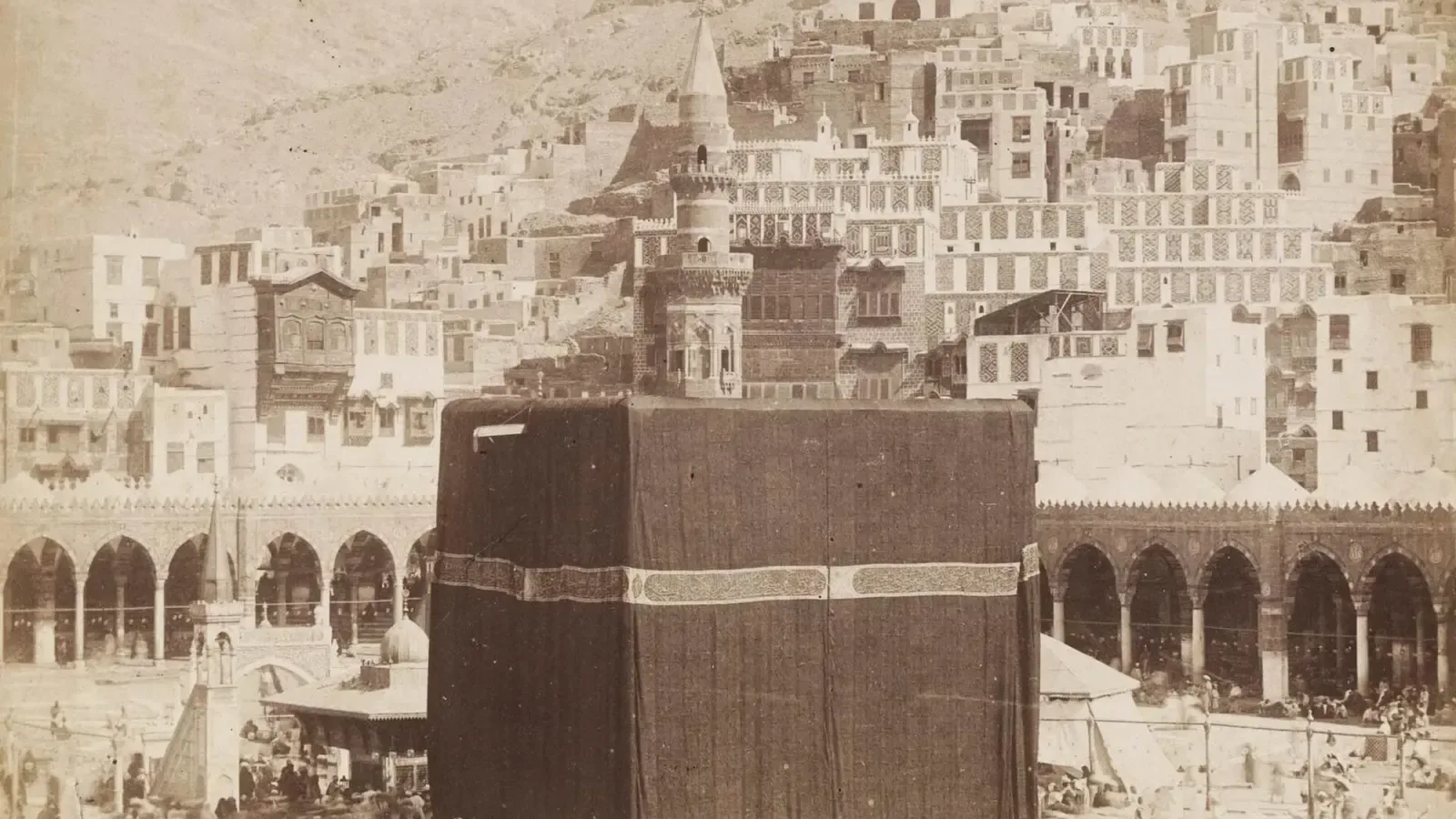 The Kaaba in Mecca, covered in its black cloth, with the arcades of the Sacred Mosque and the city behind it