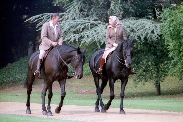 La reina Isabel II a caballo, con un pañuelo en la cabeza atado bajo la barbilla, junto al presidente Reagan